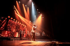 A singer performs on an orange-lit stage at IU Auditorium.